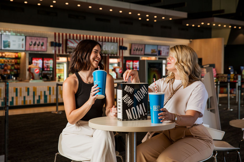 Two girls inside cinema with drink and popcorn